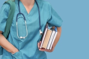 Close up of a medical student in scrubs with a stethoscope and books